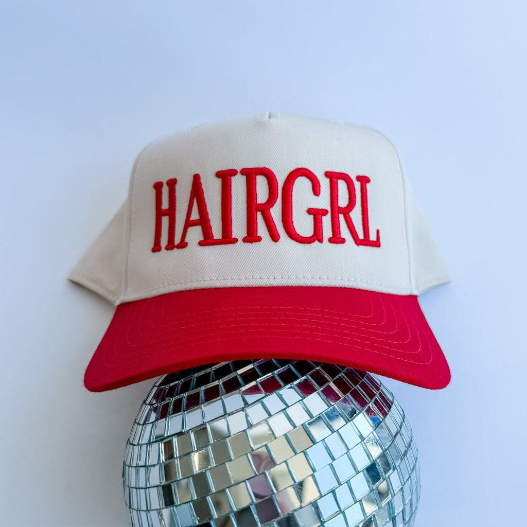 Beige and red cap with 'HAIRGRL' text on a disco ball against a light blue background