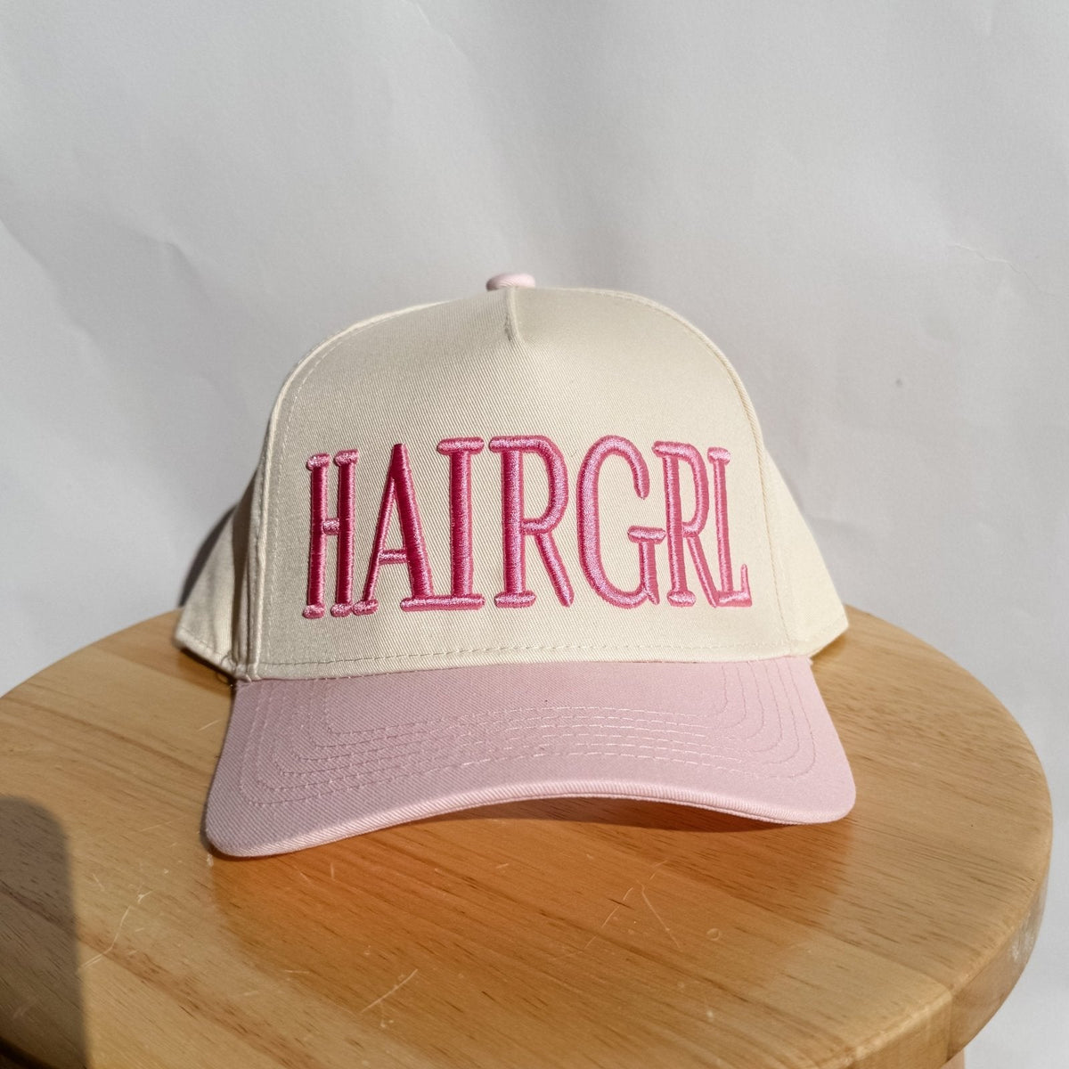 Beige and pink cap with 'HAIRGRL' text on a wooden surface